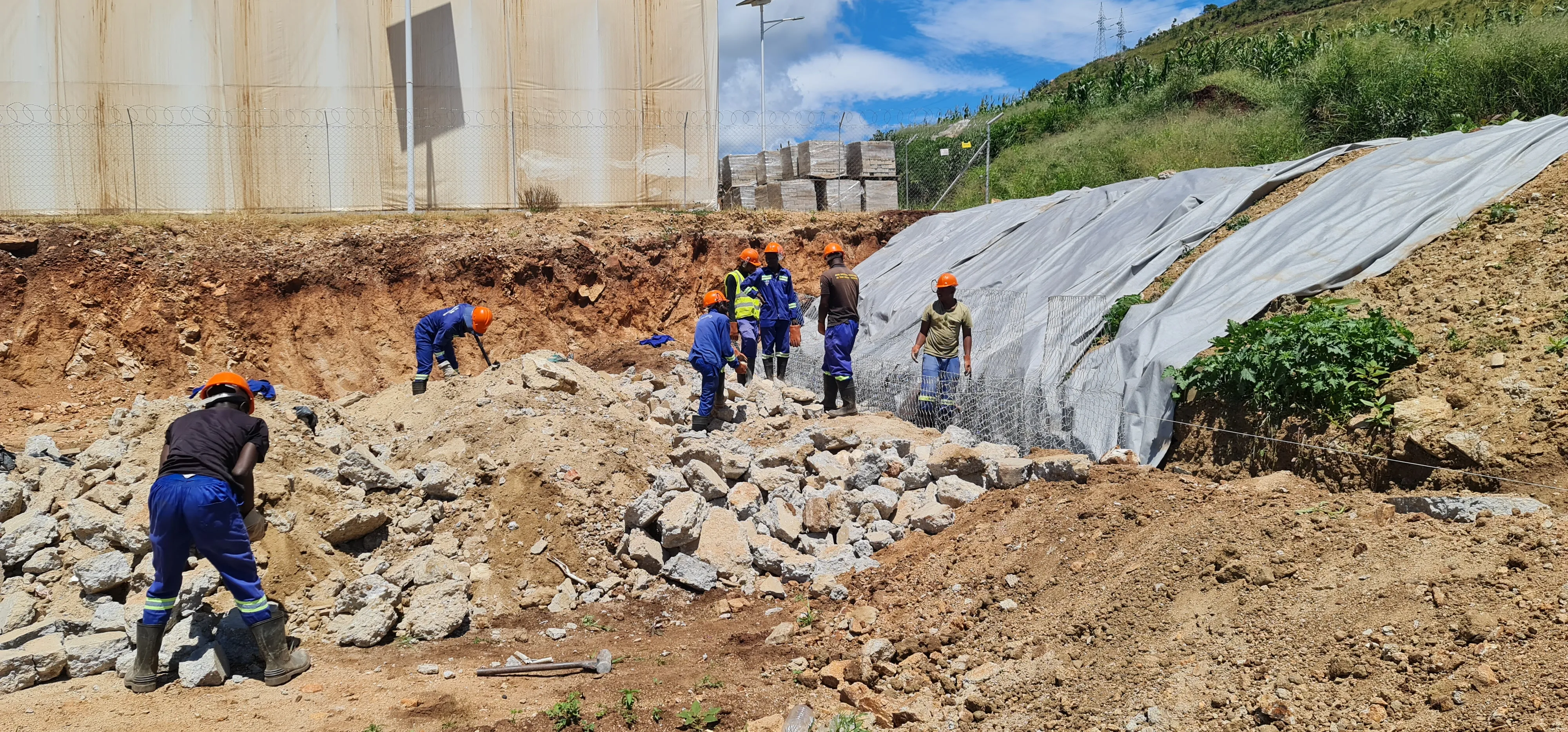 Professional construction team of diverse workers in hard hats and safety gear reviewing blueprints on construction site with modern building in background